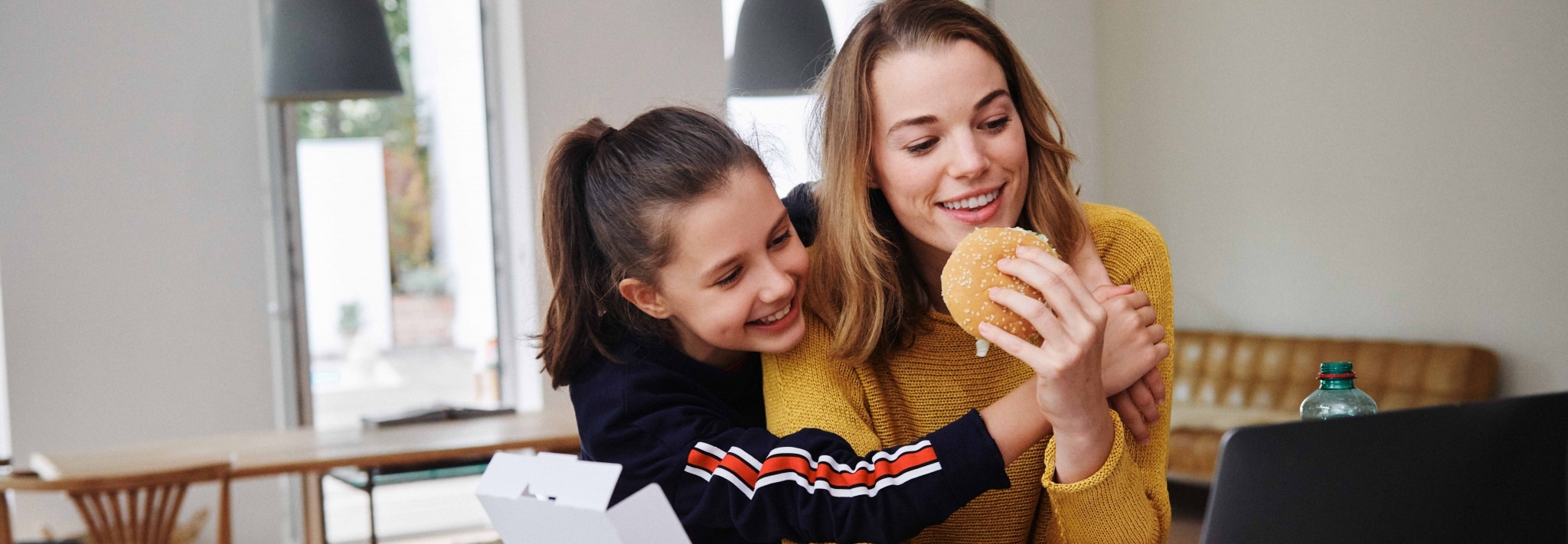 Zwei junge Frauen sitzen mit McDonald's-Burger vor Laptop