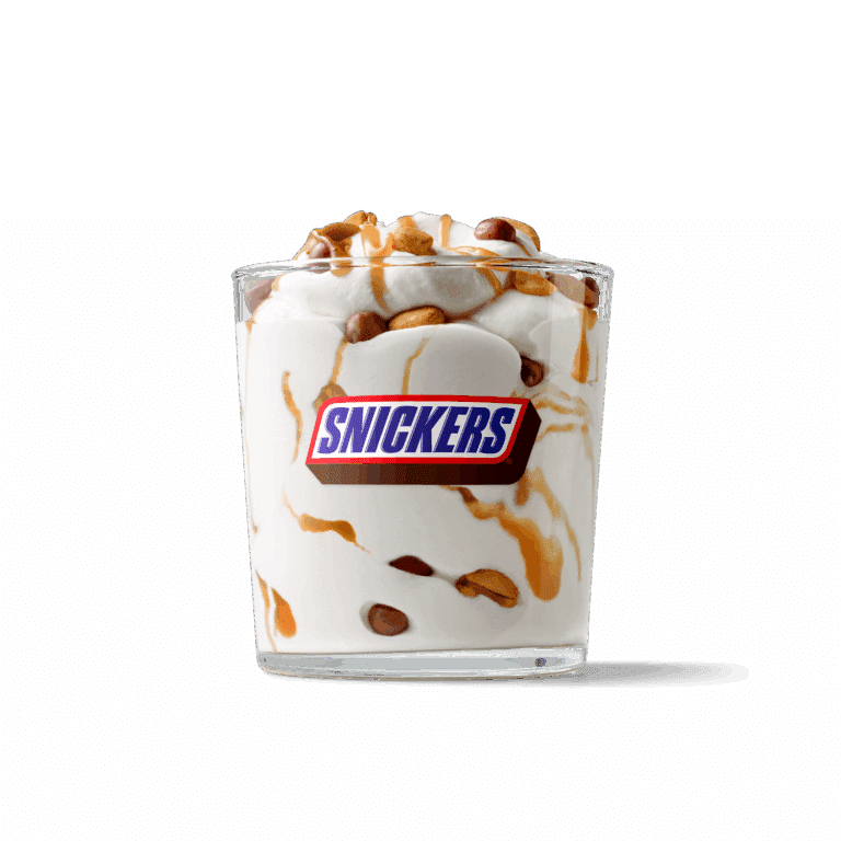 Ein Becher mit Snickers-Eiscreme, garniert mit Karamell und Erdnüssen.