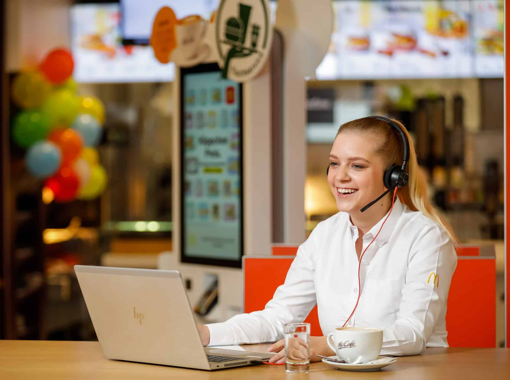 Lächelnde Frau sitzt in einer McDonalds-Filiale vor einem Laptop.