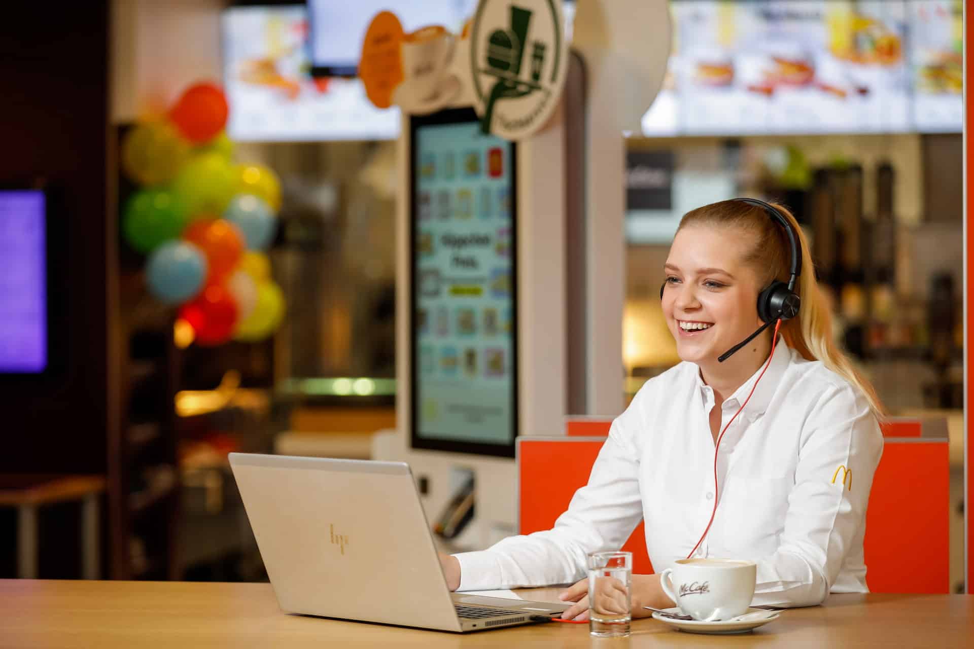Lächelnde Frau sitzt in einer McDonalds-Filiale vor einem Laptop.