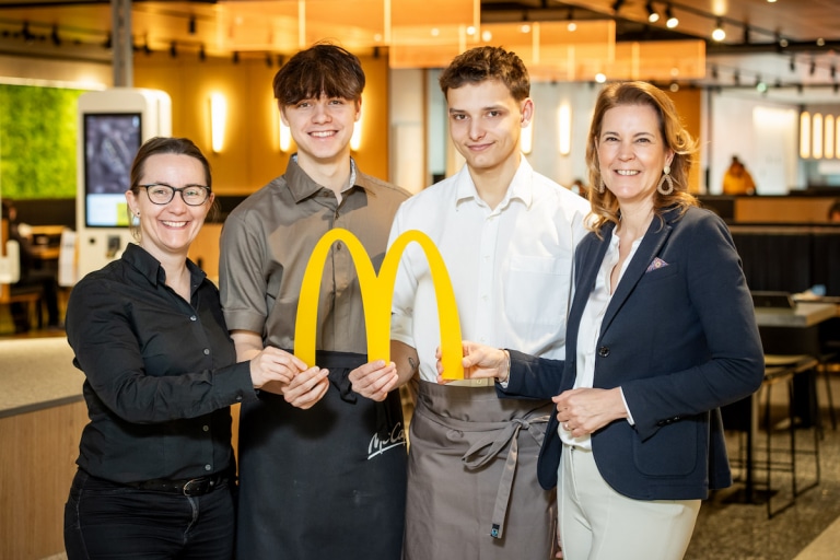 4 lächelnde Personen halten das McDonalds "M" in die Kamera.