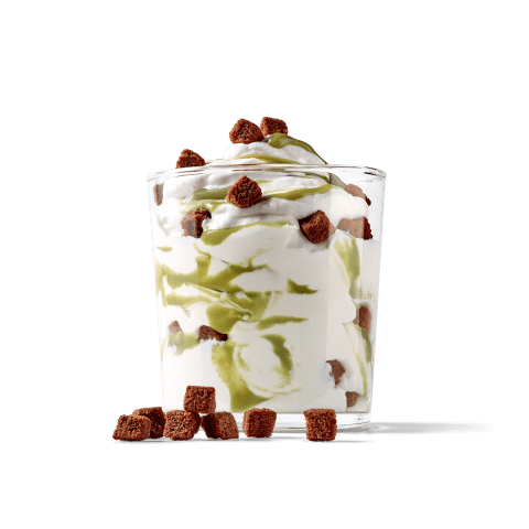 Ein köstlicher Dessertbecher mit Sahne, grüner Soße und Schokoladenstückchen auf einem grünen Hintergrund.