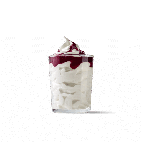 Weißes cremiges Softeis im Glas mit dunkler Heidelbeersauce als Topping.