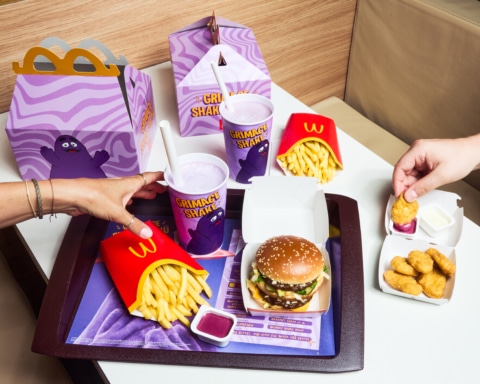 Ein Tisch mit McDonald's Essen, einschließlich Pommes frites, Burger, Chicken Nuggets und einem lila Grimace Shake.