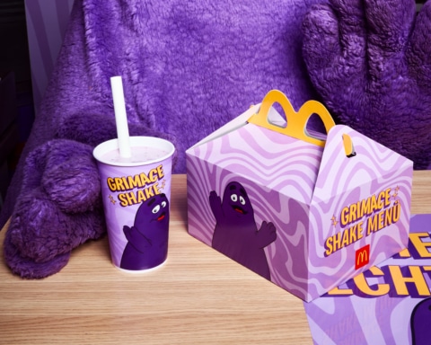 Ein lila McDonald's Grimace Shake Becher und eine Grimace Shake Menübox auf einem Holztisch.