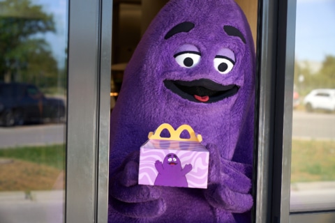 Lila Figur hält eine McDonald's Happy Meal Box am Fenster