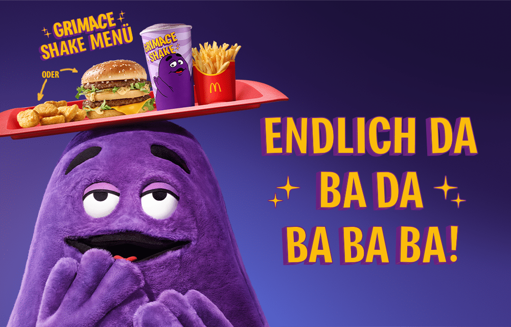 Grimace, lila, plüschiger Charakter, mit rotem Tablett auf dem Kopf. Auf dem Tablett das Grimace Shake Menü bestehend aus Grimace Shake, großen Pommes, Big Mac oder 6er Chicken McNuggets. Lila Hintergrund mit gelben Sternen.