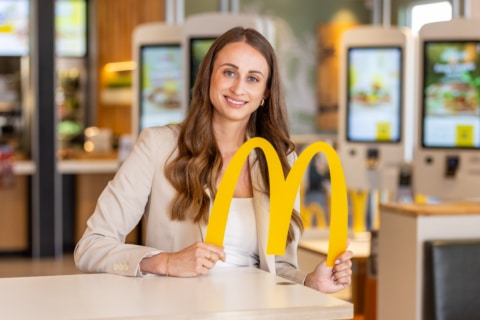Eine lächelnde Frau in einem Restaurant hält ein gelbes McDonald's Zeichen in der Hand.
