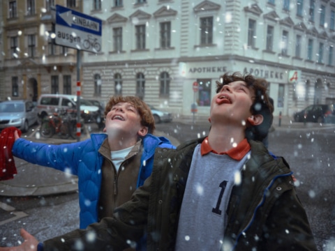 Zwei junge Jungen genießen den Schnee in einer Stadt, mit freudigen Gesichtern und geöffneten Mündern.