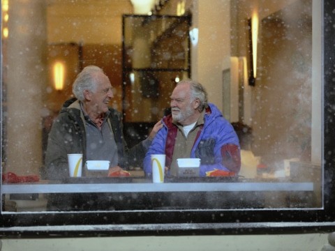 Zwei ältere Herren lachen und unterhalten sich an einem Tisch in einem Fast-Food-Restaurant während es schneit.